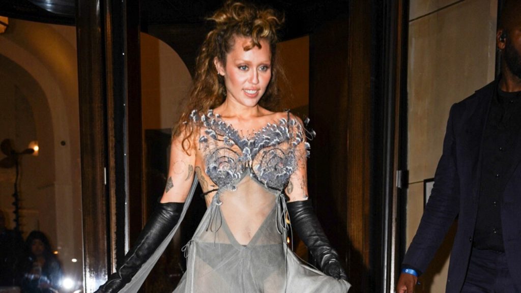 Miley Cyrus flaunts her defined abs in a sheer dress with peacock feathers in Paris.