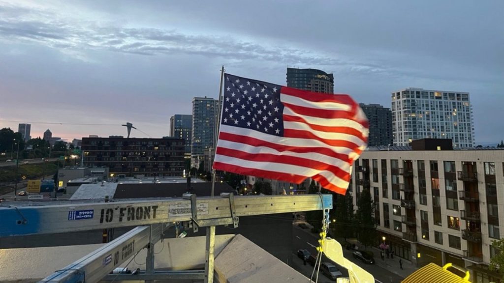 ICE officer puts up a new American flag after it was burned by protesters in Portland on July 4