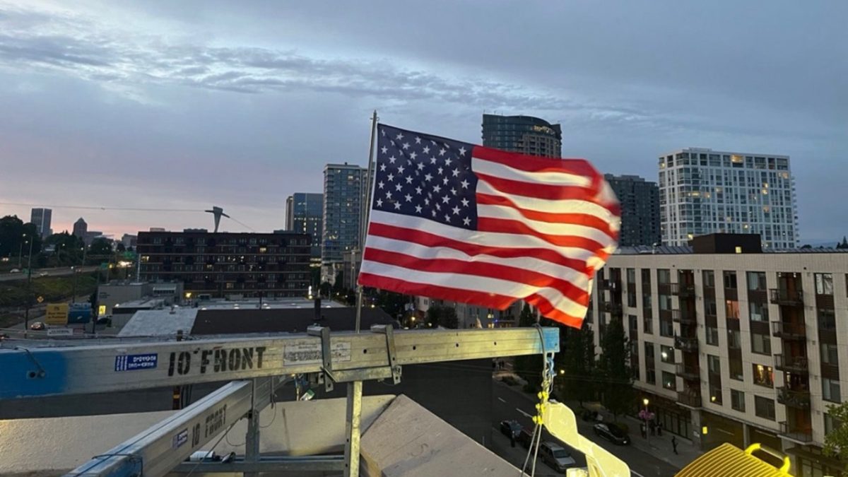 ICE officer puts up a new American flag after it was burned by protesters in Portland on July 4