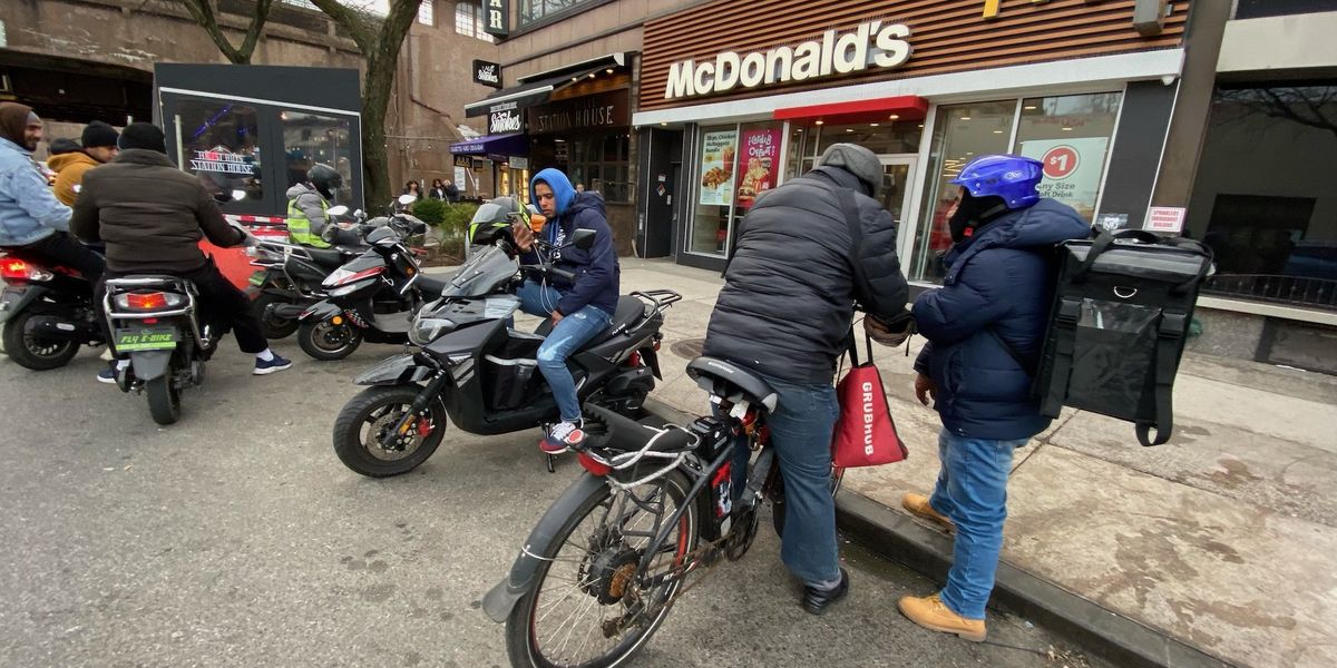 Migrant workers occupy a block in NYC using e-bikes for food delivery and night security, locals express surprise.