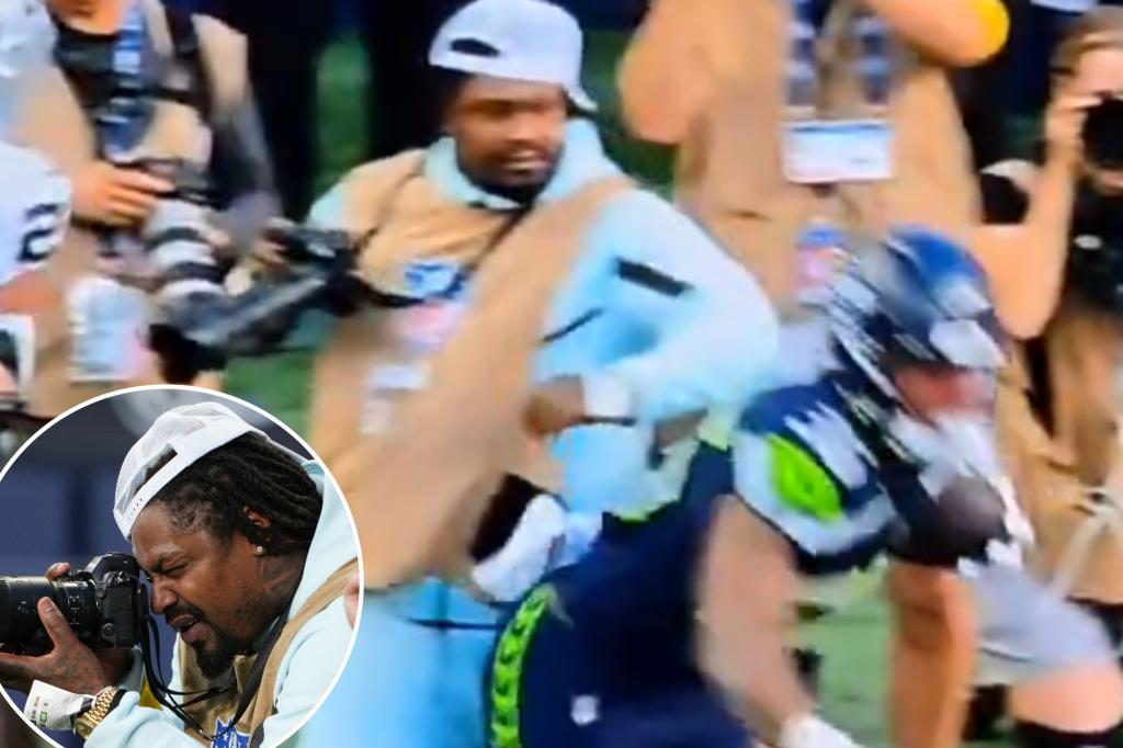Marshawn Lynch pushes away a player to guard his camera during a Seahawks preseason matchup.
