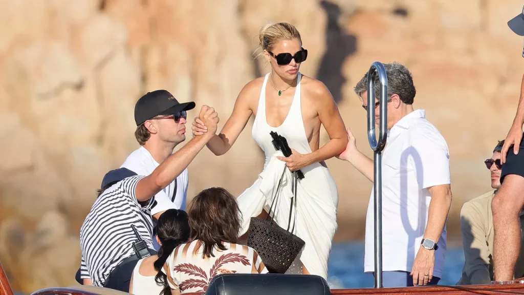 Brooks Nader enjoys a family beach day in Sardinia without her top, alongside her dad.
